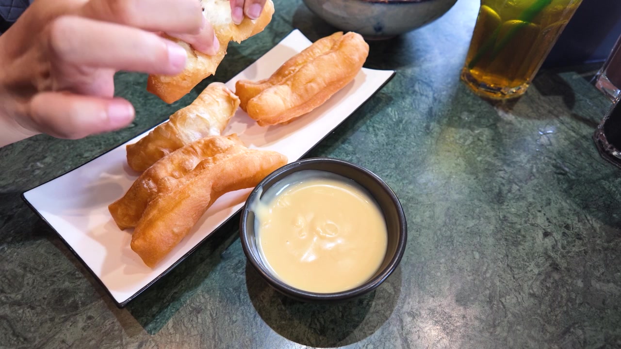 Primo piano di mani che spezzano bastoncini di pasta fritta dorati serviti con salsa cremosa alla vaniglia per intingere