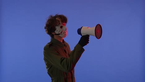 man in white mask with loudspeaker in hands on blue background with red neon light image of maniac - man in white mask with loudspeaker in hands on blue background with red neon light. image of maniac jason voorhees from friday 13. he is saying something. halloween celebration concept