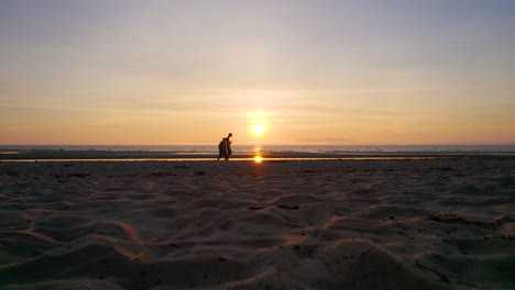 Couple-walk-along-a-beach-on-the-west-coast-of-Scotland-silhouetted-by-a-beautiful-sunset