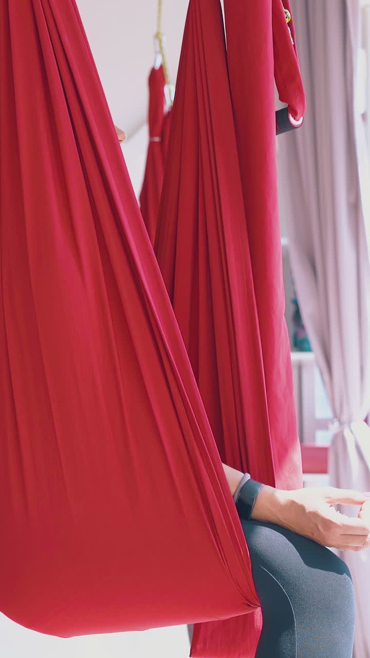 relaxed women sit and meditate in butterfly fly yoga asana in special red hammocks in modern gym close view
