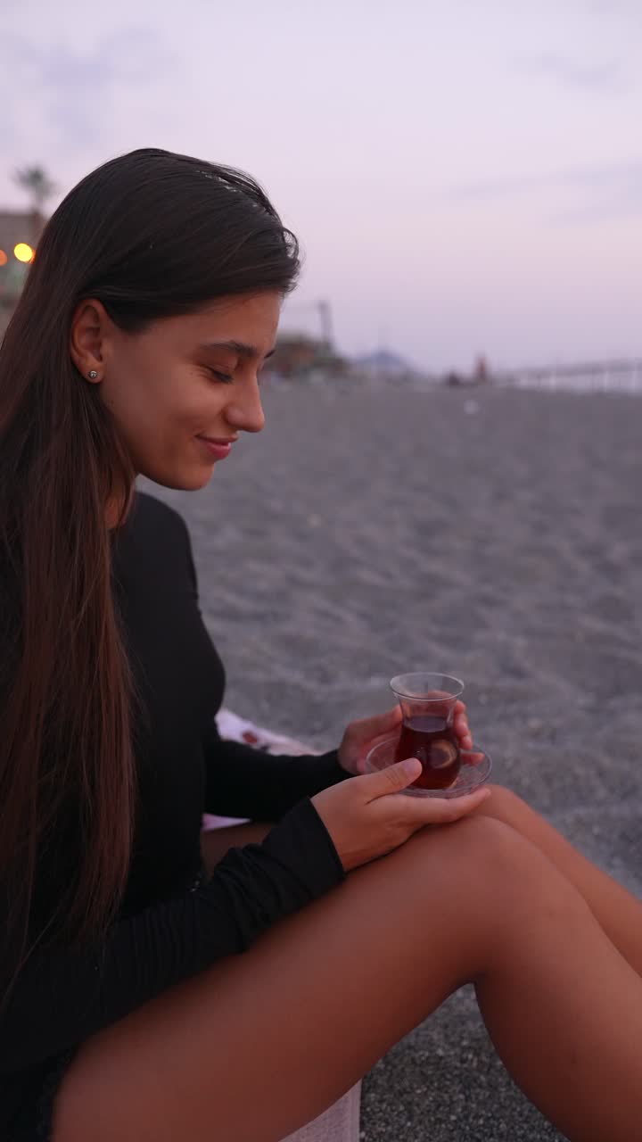 Mulher apreciando chá turco na praia ao pôr do sol
