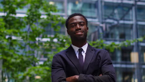 Portrait-Of-Confident-Smiling-Young-Businessman-Wearing-Suit-Folding-Arms-Standing-Outside-Offices-In-The-Financial-District-Of-The-City-Of-London-UK