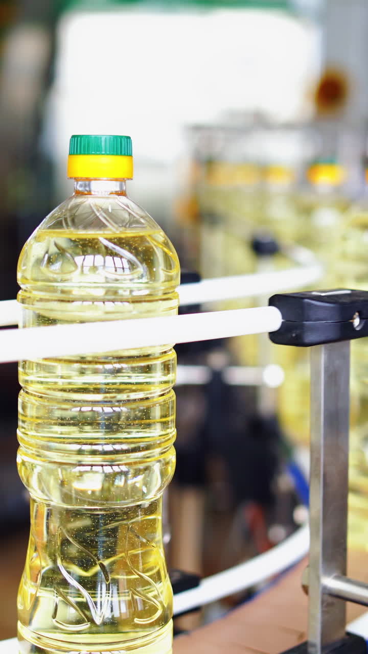 Motion of oil bottles in a modern plant. Full plastic bottles with sunflower oil moving on a conveyor line. Automated factory background of olive oil production. Vertical video