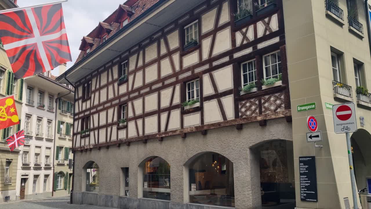 Revealing shot of traditionally built, timber-framed houses in Bern’s old town, Switzerland. Wooden beams crisscross the facades as flags gently sway in the breeze on a calm spring morning