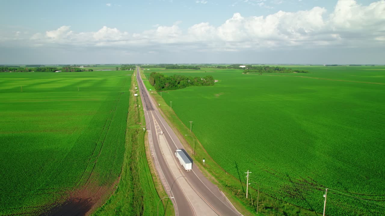 Aerial shot of a roundabout in rural Minnesota farmland, showing a dry van semi-truck and cars traveling through green fields.