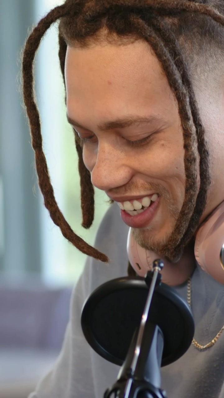 Vertikal video: Vuxen man lutar sig mot mikrofonen på signal i hemmastudio med popfilter, rosa hörlurar