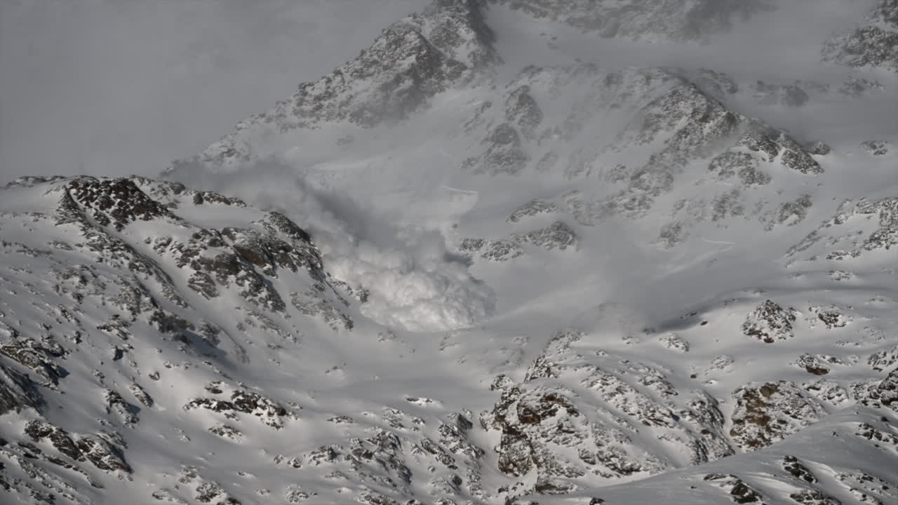 View of an avalanche rolling down a snowy mountain in the Swiss alps in Saas Fee, raised snow fog, science phenomenon