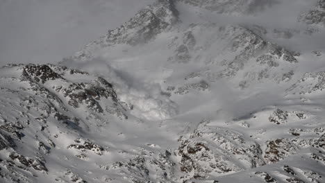 View-of-an-avalanche-rolling-down-a-snowy-mountain-in-the-Swiss-alps-in-Saas-Fee,-raised-snow-fog,-science-phenomenon