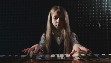 child plays piano during music lesson. tiny girl artist engages with musical device in sound recording studio. children talent musical advancement