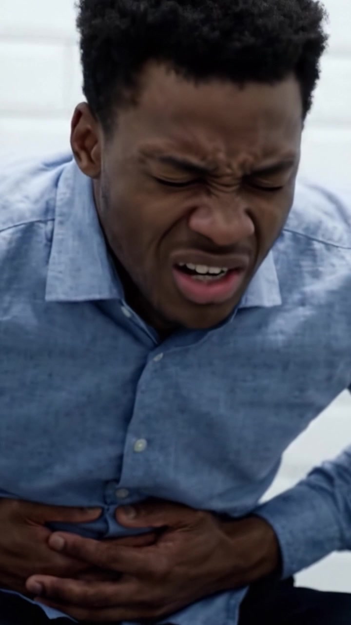A Young Man Experiencing Severe Discomfort and Pain in His Abdominal Area, Evident in His Expression and Body Language in a Constrained Situation