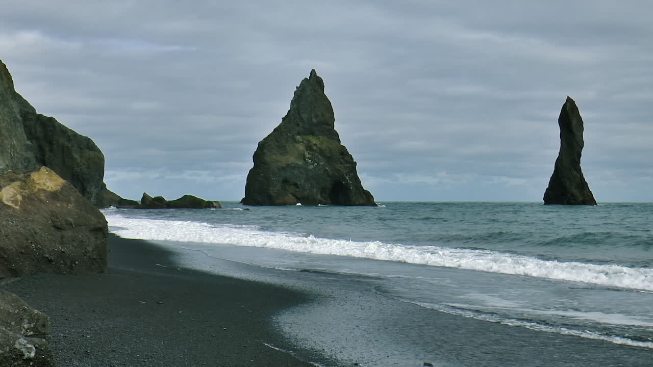 imágenes en cámara lenta de las olas del océano en la playa de arena negra reynisfjara con reynisdrangar - rocas marinas de basalto situadas bajo la montaña reynisfjall, cerca de la aldea de vik i myrdal en islandia