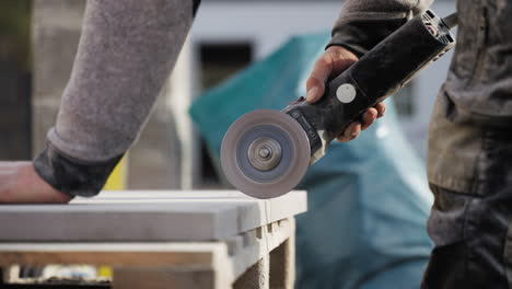 a man using a power tool - an angle grinder to cut a piece of wood material outdoors at the construction site