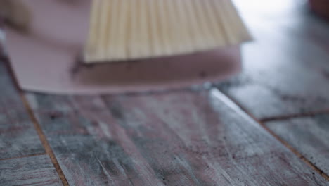 close up view of hand using brush to pack dark potting soil into dustpan on tiled floor, highlighting detailed cleaning motion and careful debris collection in cozy indoor environment