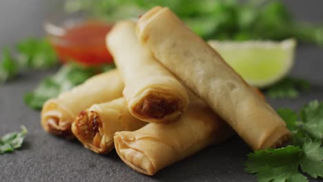 composition of plate with spring rolls and chilli sauce on black background