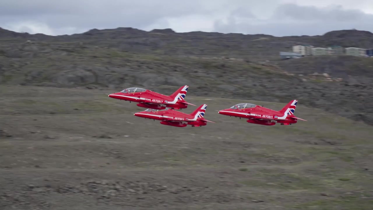 Telephoto tracking shot showing three RAF Red Arrows BAE Hawk jets taking off simultaneously in parallel formation, flying past the camera from right to left.