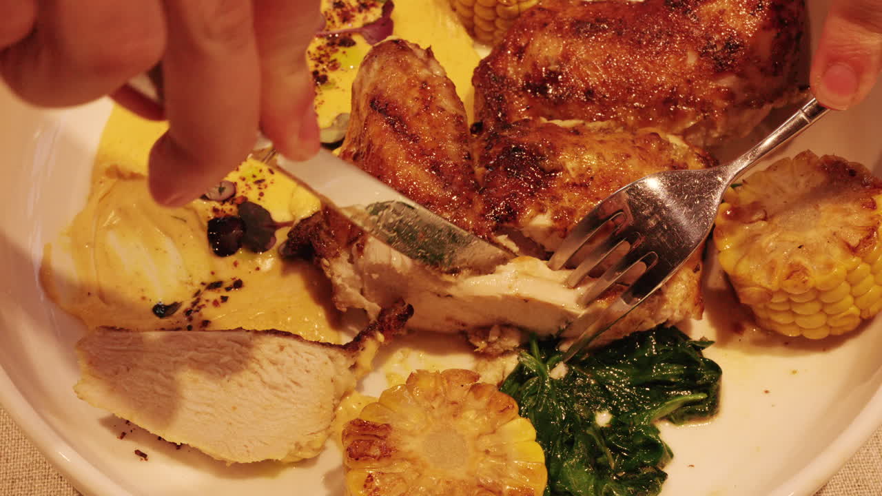 Primo piano di mani che tagliano un piatto di pollo grigliato con forchetta e coltello