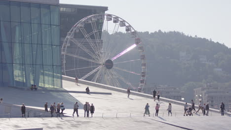 people walking outside oslo opera house with view of opera ferris wheel in back