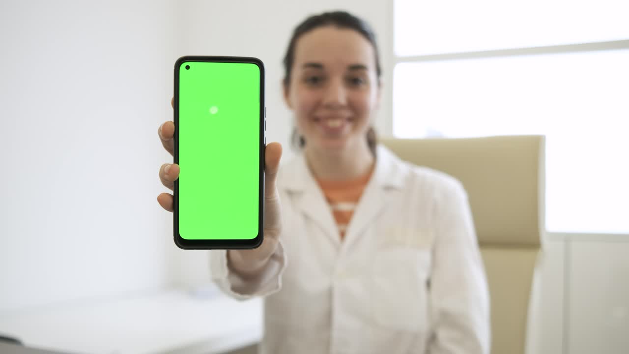 Cheerful female doctor showing smartphone with green screen