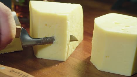 three cheeses on cutting board, small knife cuts slice of gouda block