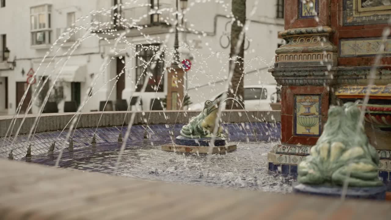 Scenic view of traditional fountain with frog statues spewing water up, residential buildings in background