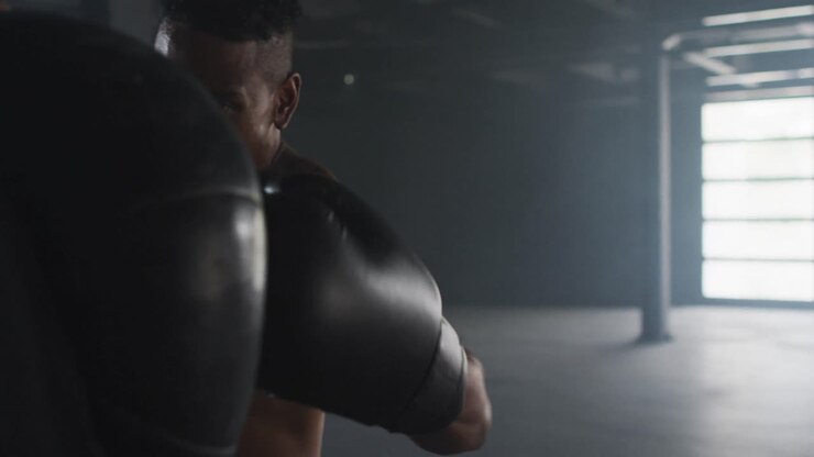 Uomo afroamericano con i guantoni da boxe che si allena in un edificio vuoto, colpendo il sacco da boxe.