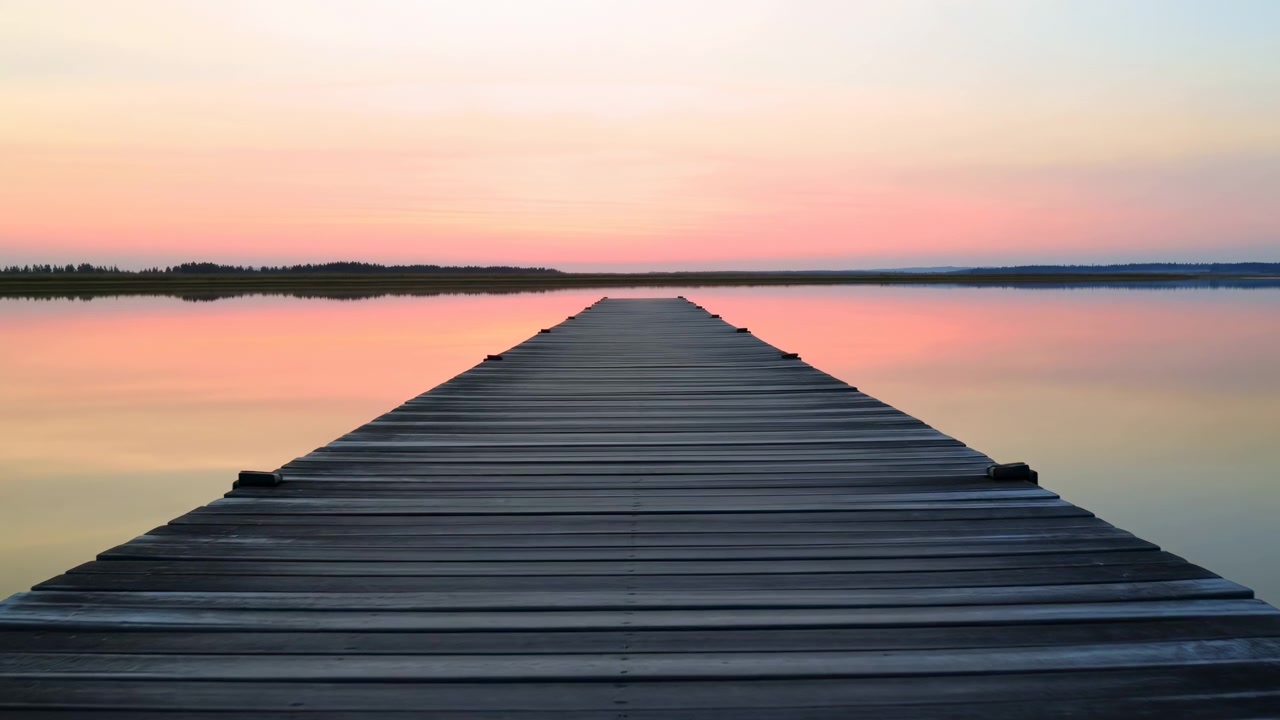 Una tranquilla scena del tramonto con un pontile di legno che si riflette su acqua calma, circondata da un ambiente sereno in riva al lago o al fiume, immersa in tonalità rosa e arancioni, catturata da una prospettiva grandangolare fissa