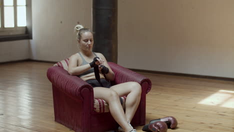 long shot of focused woman wrapping fists with bandage in gym