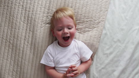 Mom-tickles-the-boy-lying-on-the-bed-who-looks-directly-into-the-camera-and-laughs-loudly