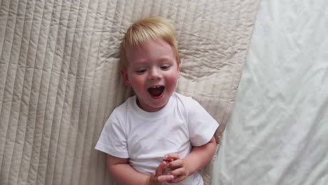 mom tickles the boy lying on the bed who looks directly into the camera and laughs loudly