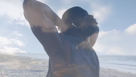 Animation-of-clouds-over-exercising-african-american-man-stretching-on-beach