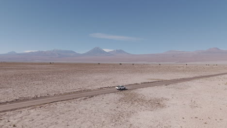 drone shot flying over the dry sand desert mountains in san pedro de atacama chile south america on a blue sky day with a white truck driving along near mars valley and valley de la luna log