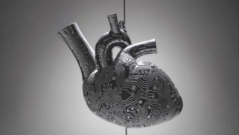 artificial metallic heart with visible circuitry hanging on a wire against a gray background, symbolizing medical technology and innovation