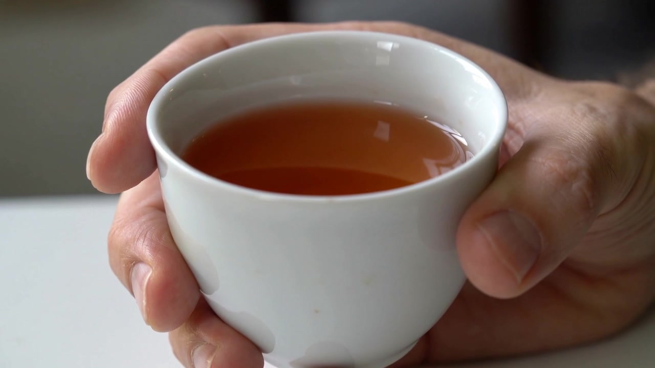 La cámara enfoca, un hombre sostiene una taza firmemente sobre la mesa para mantener las manos calientes con té ámbar