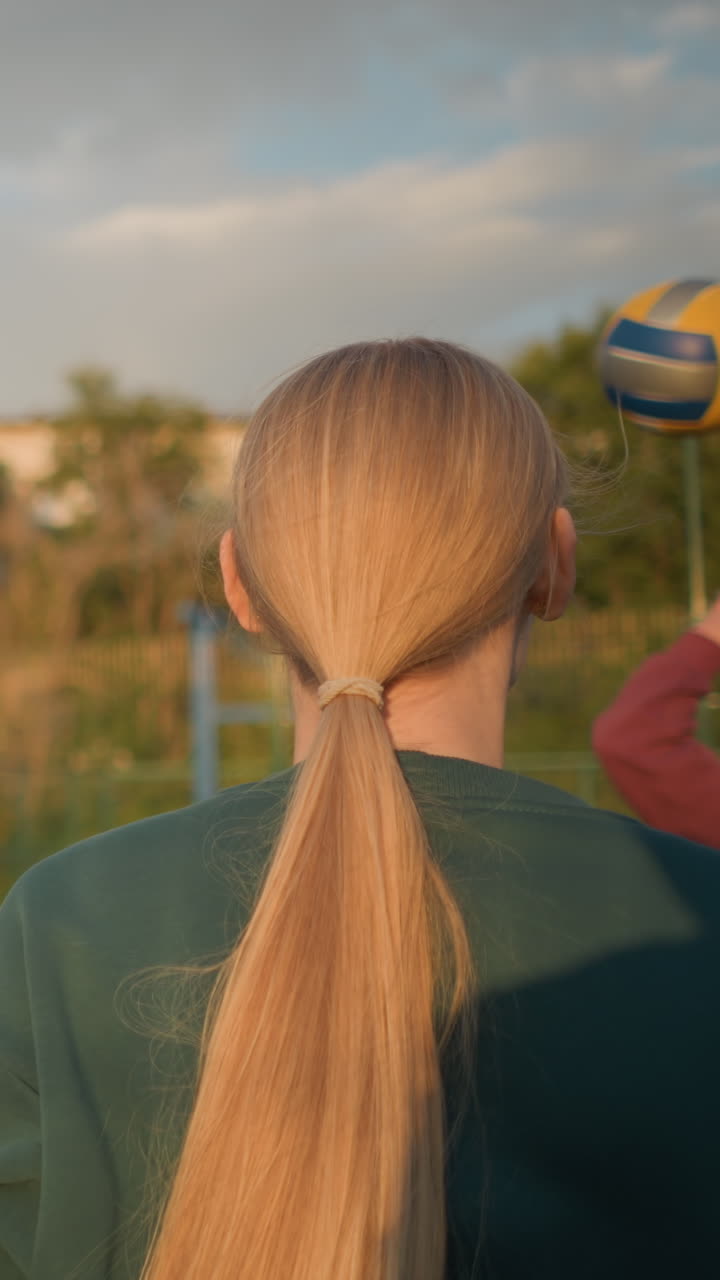 푸른 스웨터를 입은 선수가 배경에 흐릿하게 보이는 파란 스웨터에 다른 선수와 함께 볼리볼을 하는 뒷면, 이 밝은 야외 세션 중에 배경에 보이는 건물