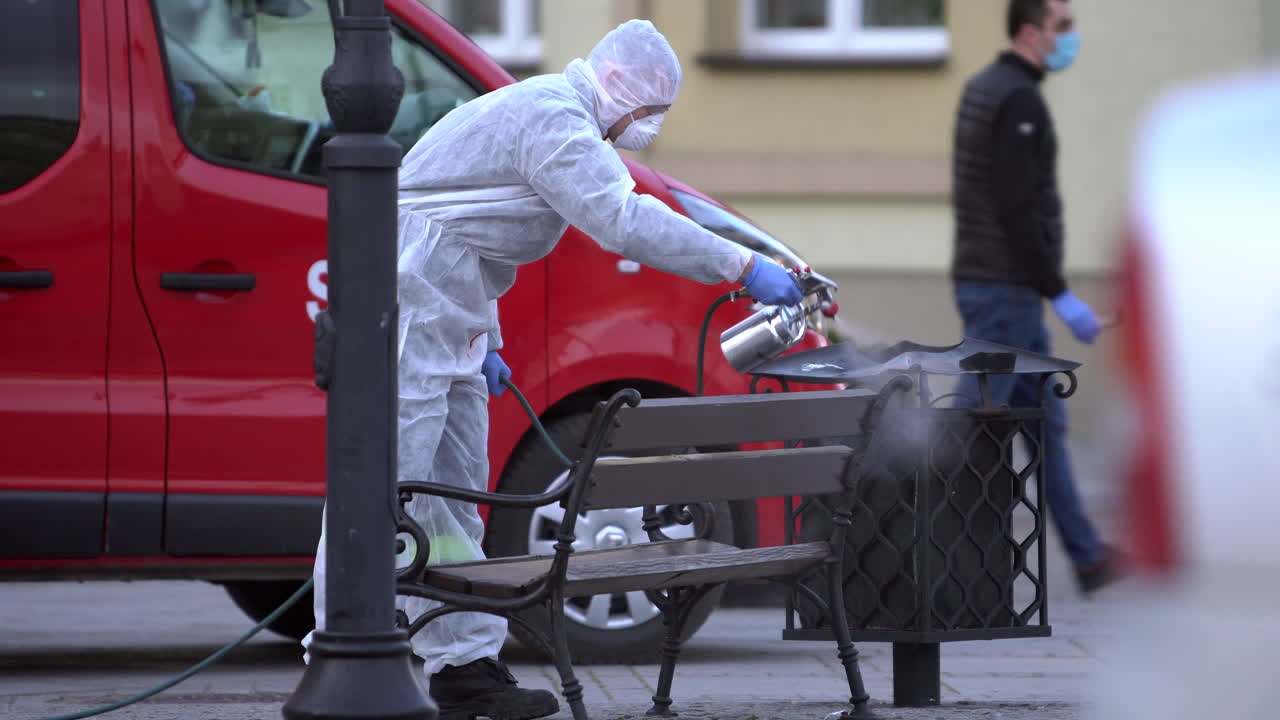 Fireman in protective suit disinfects a public bench on market square.