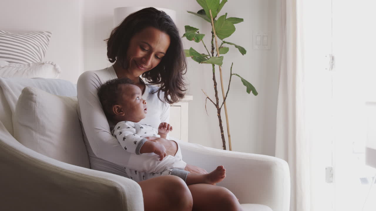 Happy millennial African American mother sitting in rocking chair holding her baby