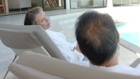 Relaxing by pool, senior couple lounging on chairs, enjoying vacation time