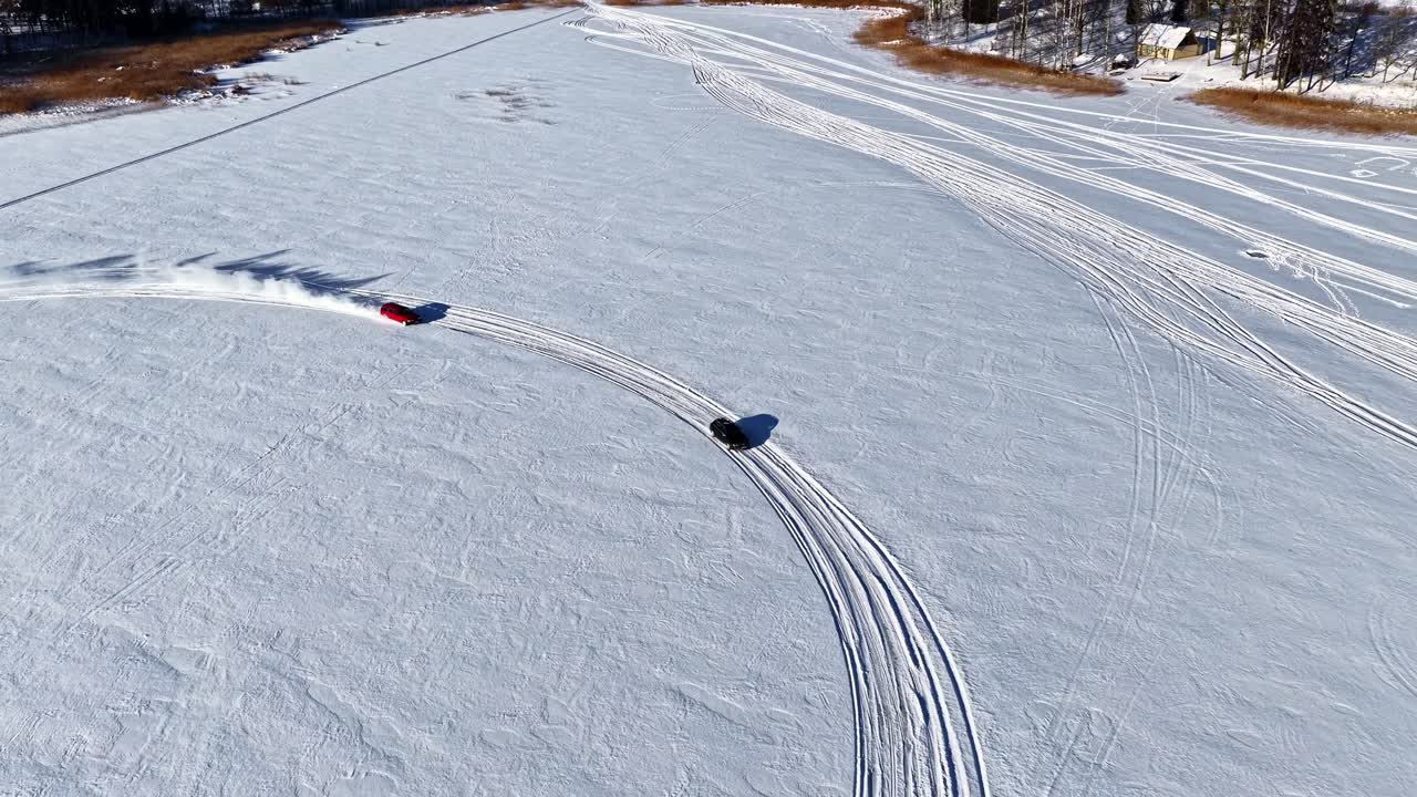 Drone riprende un'auto che sbanda su un ampio campo innevato sotto un cielo azzurro limpido, in pieno sole invernale