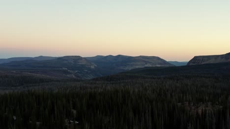 beautiful left trucking aerial drone shot of the stunning wild uinta wasatch cache national forest in utah with trees below and large pointy rocky mountains on a misty summer morning
