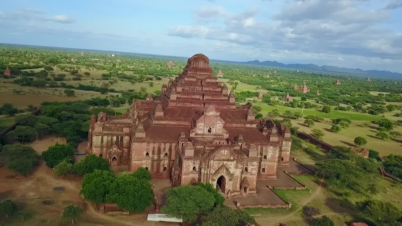 A breathtaking drone pull-out revealing the sprawling temple-studded landscape of Bagan, Myanmar, with the First Temple standing out amid lush greenery and historic beauty