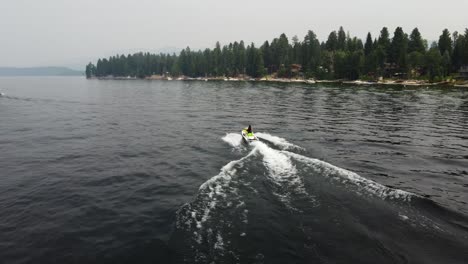 disparo de un dron siguiendo a una persona que conducía una moto de agua en el lago payette en mccall, idaho con la orilla y los árboles en el fondo
