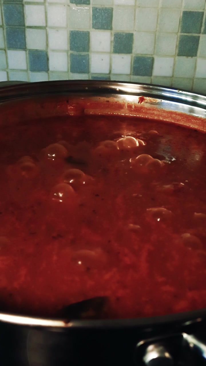Primo piano di una vivace zuppa di pomodoro rosso che sobbolle e ribolle in una pentola di acciaio inossidabile su un fornello, perfetta per mostrare la cucina casalinga, il comfort food e i processi culinari.