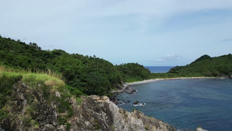 Aerial-View-of-Breathtaking-Island-Cove-with-jagged-coastline-rocks,-turquoise-ocean-waters,-and-white-sand-beach