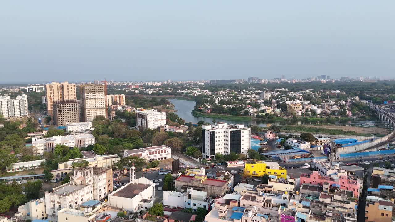 A panoramic aerial view reveals urban layers. featuring a white bell-tower. A winding river on the right provides a natural boundary to this sprawling, developing city. Adyar River and Saidapet bridge