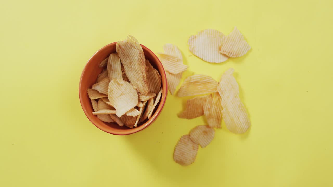 Close up of potato chips falling in a bowl on yellow surface