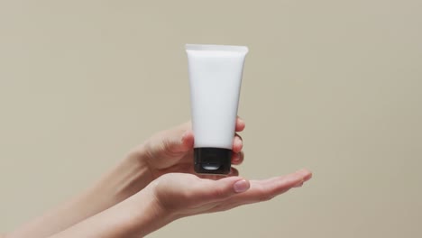 hands of woman holding tube with cream on beige background with copy space, slow motion