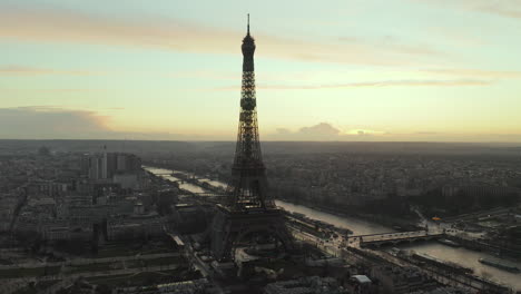 Slide-and-pan-aerial-shot-of-amazing-historic-steel-structure-of-Eiffel-Tower-and-Seine-river-flowing-around.-City-at-dusk.-Paris,-France