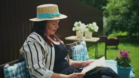 woman in striped jacket wearing straw hat reading book outdoors in a serene garden setting