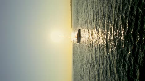 vuelo aéreo vertical hacia atrás que muestra la silueta de un yate catamarán de lujo en el océano con una puesta de sol dorada en el horizonte