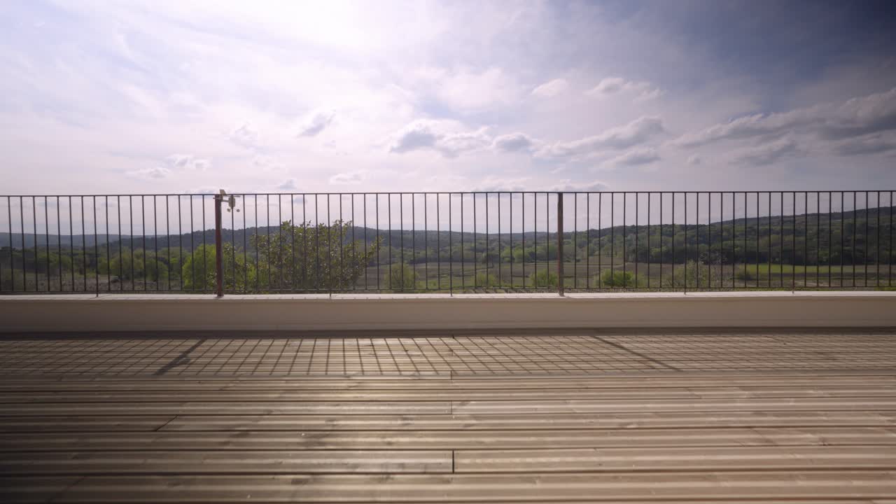 disparado que conduce a través de una terraza con suelo de madera a cercas metálicas para llegar a una gran vista de viñedos, campos y naturaleza, horizonte, cielo y nubes